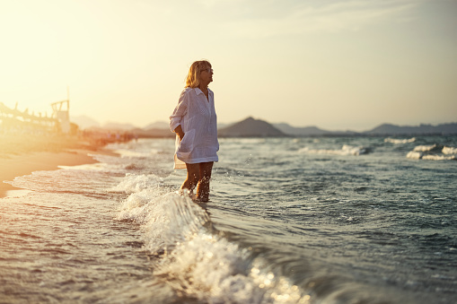 Senior woman enjoying sea vacations. The woman is walking on the beach.\nCanon R5
