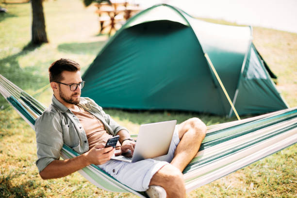 istock Mid adult man using smart phone and laptop while relaxing in hammock in nature. 1346583105