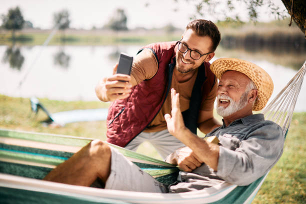 happy man and his senior father making video call over smart phone while spending a day in nature. - fishing active seniors family senior adult imagens e fotografias de stock