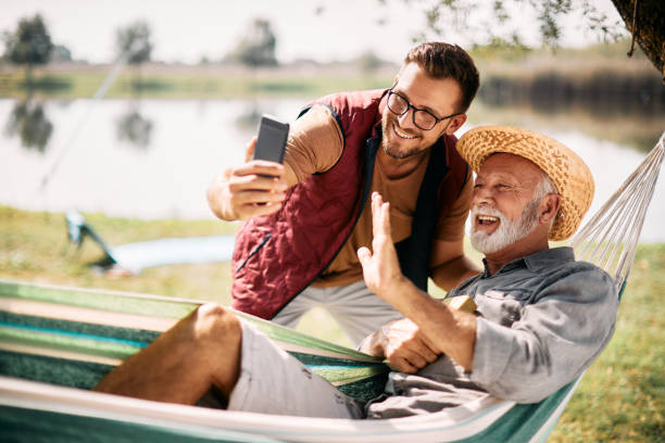 счастливый мужчина и его старший отец делают видеозвонок по смартфону, проводя день на природе. - fishing active seniors family senior adult стоковые фото и изображения