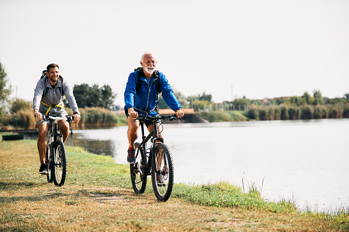 Happy mature athletic man and his son enjoying in cycling by the lake. Copy space.