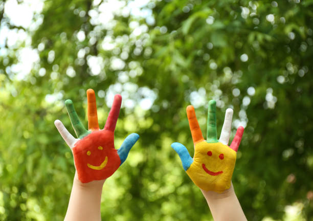 istock Kid with smiling faces drawn on palms in green park, closeup 1346585177