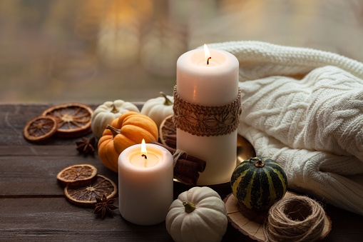 Autumn composition with candles, mini munchkin pumpkins, warm wool knitted plaid on the wooden wind sill. Dark colors, low key. Cozy home atmosphere, Thanksgiving decor, fall colors. Close up