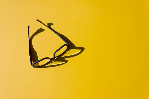 istock Stylish glasses with reflection and sunshine shadow on bright yellow background. 1346592470
