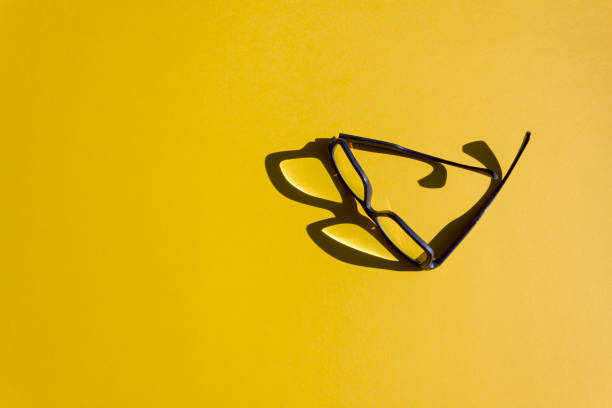 istock Stylish glasses with reflection and sunshine shadow on bright yellow background. 1346592471