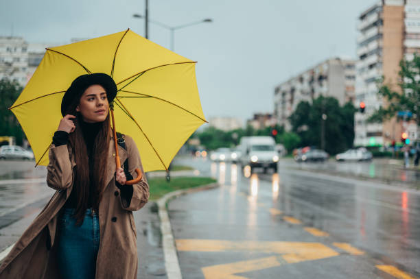 istock Young beautiful woman using a smartphone and holding a yellow umbrella 1346594462