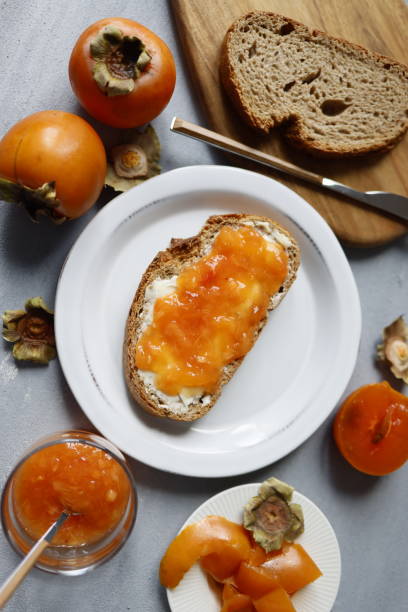 istock Persimmon paste spread on greasy bread on white plate on gray rough concrete floor, Persimmon marmalade 1346595793