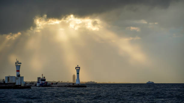 A tall lighthouse with red and white stripes stands on a rocky island, illuminating the surrounding waters as waves crash gently against the shore during twilight.
