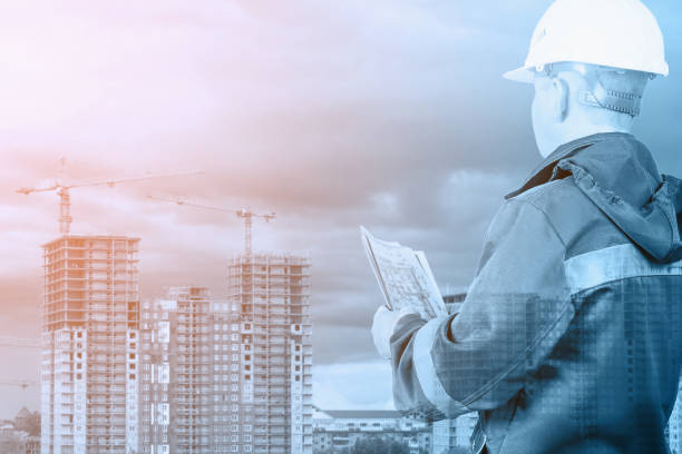 istock An engineer, architect, builder holds in his hands a plan of new buildings on the background of construction. Double exposure, collage. Selective focus. Tinted image. 1346599171