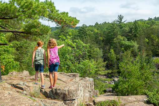 Two girls (sisters) standing on a rocky overlook at Interstate State Park in Minnesota, USA. The older sister is pointing at something in the distance.