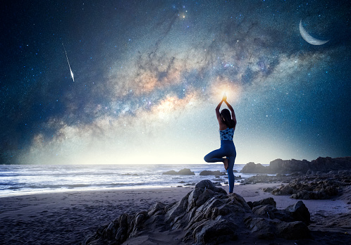 unknown woman standing in yoga tree position on the beach with Milky Way background