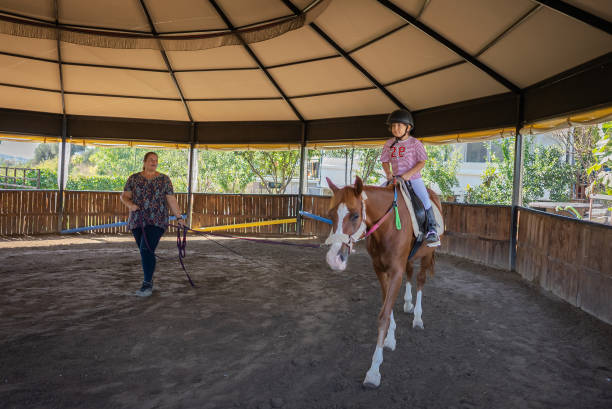 ragazza felice che si gode la lezione di equitazione in un centro privato. - teaching child horseback riding horse foto e immagini stock