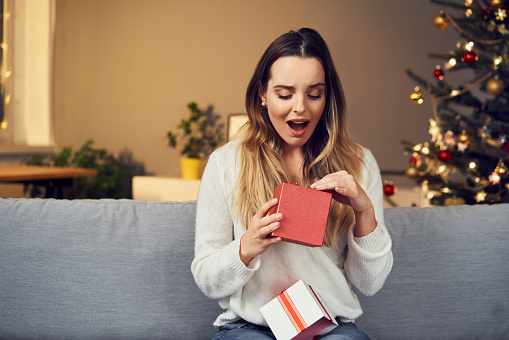 Surprised woman opening Christmas present while alone at home