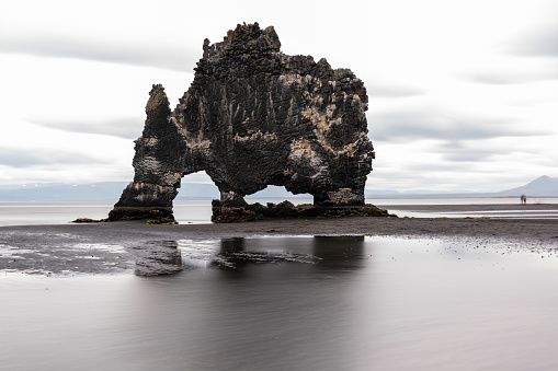 Hvitserkur is a basalt sea stack shaped like a three legged creature.  It's known as Rhino Rock or the troll rock.  It is located off the Vatnsnes Peninsula in northwest Iceland. It was formed when magma flowed into a fracture in the bedrock and filled it.  The old land surface that surrounded it eroded away.  When the magma dyke cooled, the rock fractured into horizontal columns that lie at right angles to the cooling surface.  It is about 35 feet high, but only about 5 feet thick.  Over time, the ocean's waves carved a variety of different sized hoes in the lower part of the stack.  One of the \