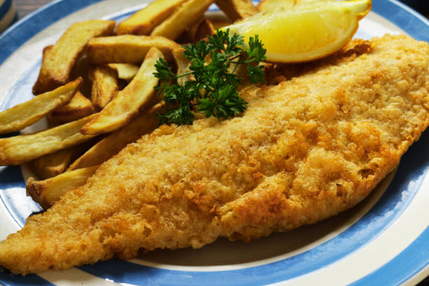 istock Full frame image of fish and chips (cod) garnished with parsley and lemon slice on blue and white Cornish ware plate, elevated view, focus on foreground 1346609177