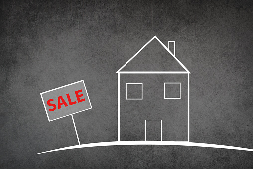 Drawing of a house on a chalkboard, the word sale is standing on the sign, textured grey background