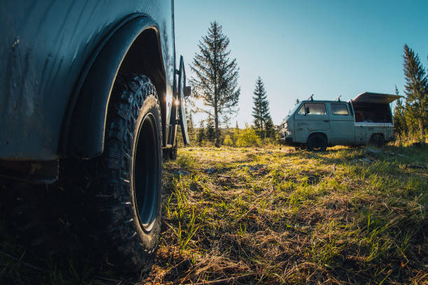 istock Two old vintage custom offroad campervans parked in the morning hours on the forest plain. View of the serious off road tire tread on a car. 1346611355
