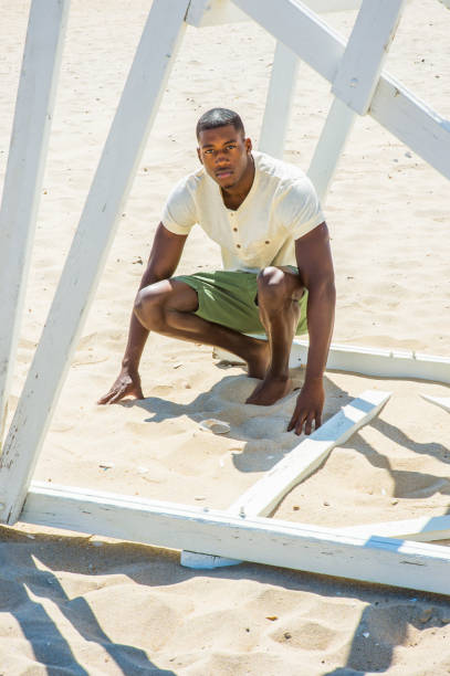 Young black man squatting on beach, relaxing