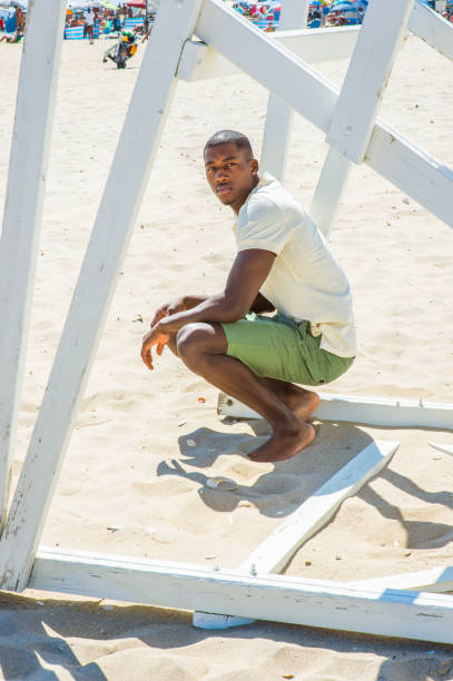 istock Young black man squatting on beach, relaxing 1346611499