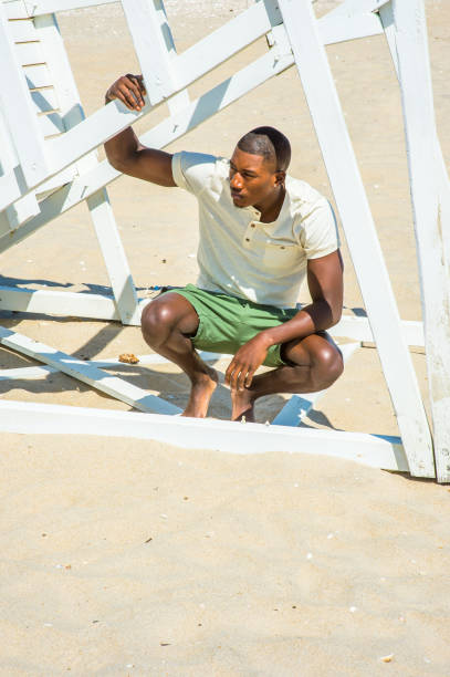 istock Young black man squatting on beach, relaxing 1346611596