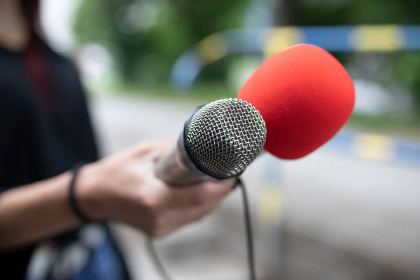Female journalist at news conference, writing notes, holding microphone