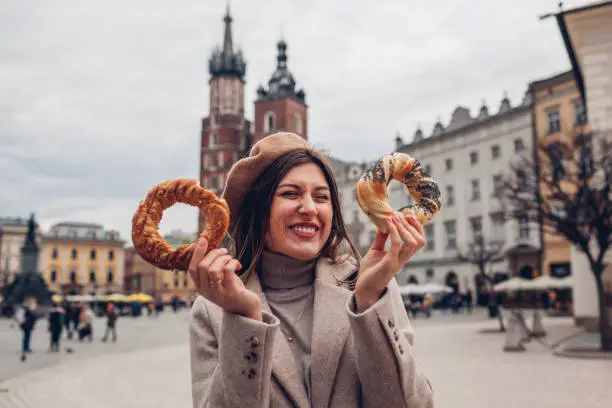 Tourist woman eating bagel obwarzanek traditional polish cuisine snack waling on Market square in Krakow. Traveling Europe in autumn