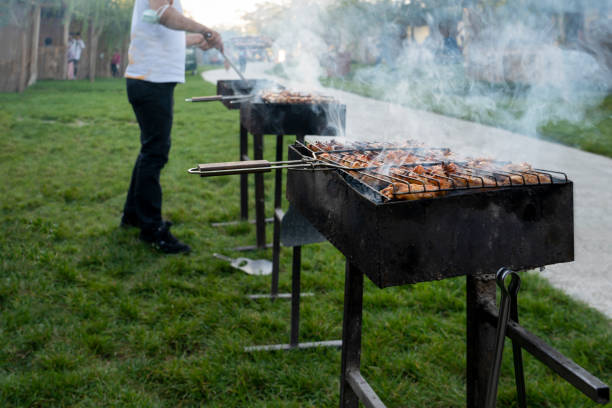 cooking chicken and meat on several barbecues with pair of tongs in hand on grass. - green steak food gourmet imagens e fotografias de stock