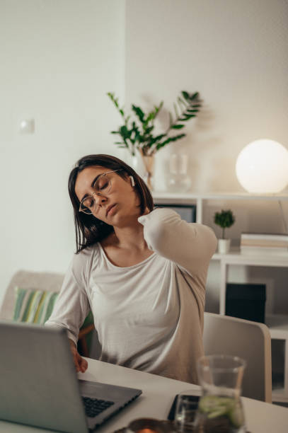istock Beautiful woman having back and neck pain while using a laptop at home 1346618747