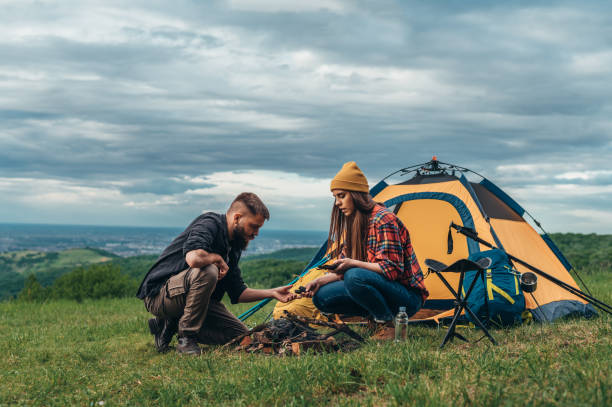 пара отдыхающих зажигает костер возле палатки в лагере - camping hiking tent couple стоковые фото и изображения