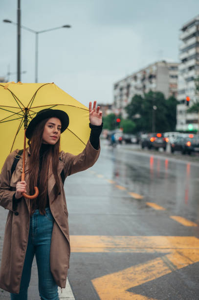 istock Young beautiful woman calling for a cab while holding a yellow umbrella 1346618769