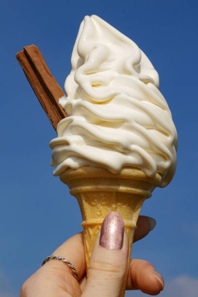 istock Image of soft-serve '99' whippy ice cream cone with chocolate-flake held by unrecognisable person on sunny day, clear blue sky background, focus on foreground 1346619966