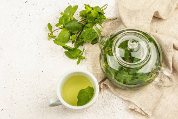 Fragrant mint tea on a light background. Glass teapot, a cup of tea, a bunch of fresh mint Fragrant mint tea on a light background. Glass teapot, a cup of tea, a bunch of fresh mint. Good morning concept, top view mint tea stock pictures, royalty-free photos & images