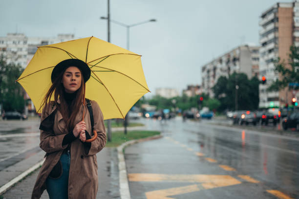 istock Young beautiful woman using a smartphone and holding a yellow umbrella 1346621944