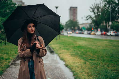 Beautiful woman walking in the park while holding a black umbrella during rainy day