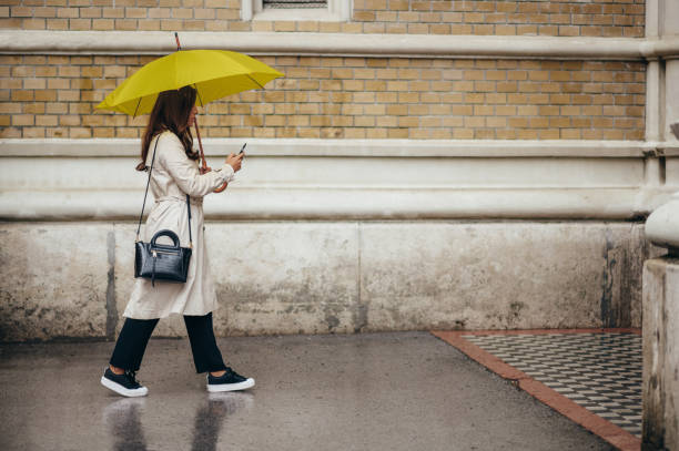 kobieta korzystająca ze smartfona i trzymająca żółty parasol podczas pobytu w mieście - umbrella women storm yellow zdjęcia i obrazy z banku zdjęć
