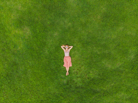 Young woman lying down in the middle of a field and relaxing, drone photo.