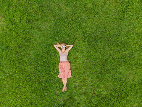 Young woman lying down in the middle of a field and relaxing, drone photo.