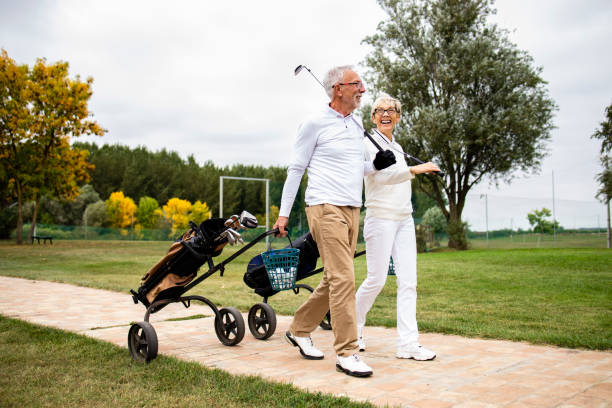 ein elegantes seniorenpaar, das die freizeit im ruhestand genießt, indem es golf spielt und zum übungsplatz geht. - retirement golfer happiness relaxation stock-fotos und bilder