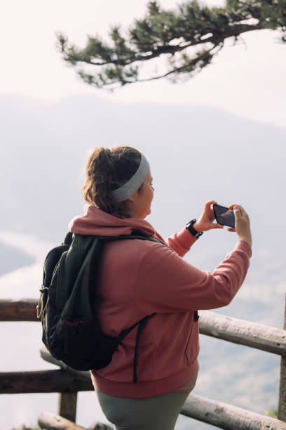 mujer excursionista de pie en un mirador de alta montaña y tomando una fotografía en un teléfono móvil - splash mountain fotografías e imágenes de stock