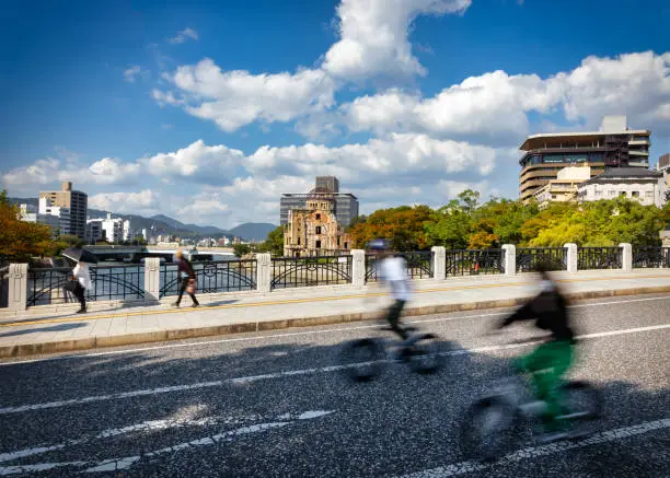 Bicylists and pedestrians cross the Motoyasu River Bridge passing the ruins of the Atomic Bomb Dome near atomic bombs ground zero in Hiroshima, Japan.