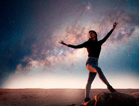 latin woman is dancing or posing on the top of the mountain at night with Milky Way as a background and shooting star