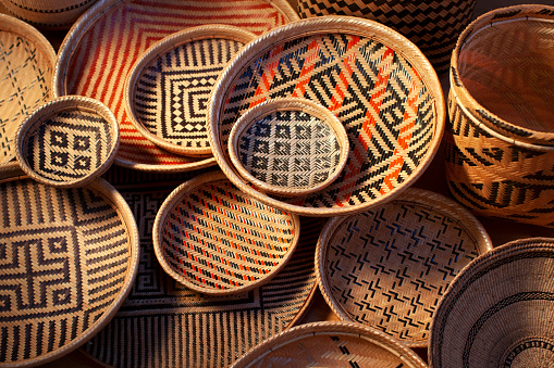 A small, round, handmade African basket on a white background. The basket is open, with the lid leaning against it.