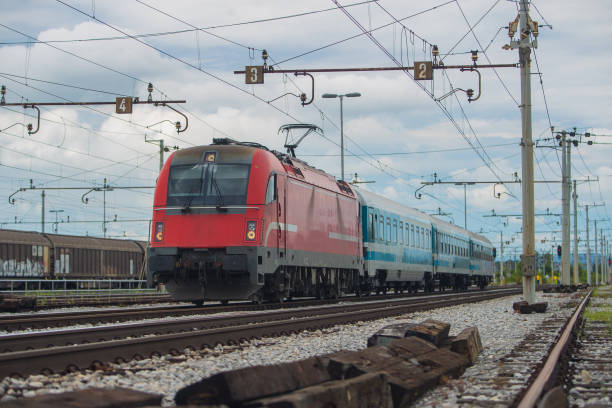 istock Modern electrical train  with red engine on track on a suburban station. Passenger train rushing towards the city in a suburban environment on a cloudy day. 1346669526