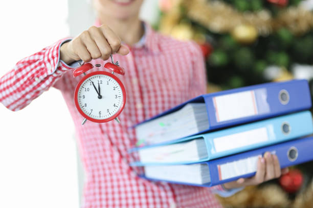 여자는 12시 알람 시계를 보유하고 크리스마스 트리의 배경에 대한 문서의 스택 - santa claus christmas watch workshop 뉴스 사진 이미지