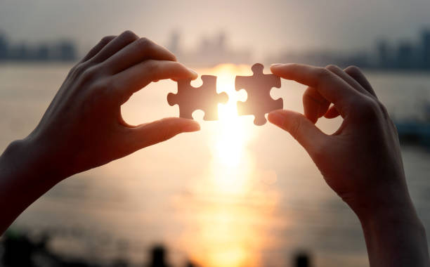 Human hands put two jigsaw puzzle pieces together.