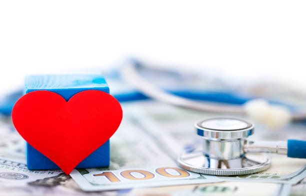 Close-up of a red heart with a stethoscope on a heap US $100 dollar bills in the background. Shallow depth of field, space for copy.
