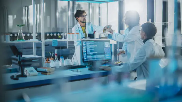 Photo of Modern Medicine Research Laboratory: Diverse Team of Multi-Ethnic Young Scientists Passes Samples in Petri Dish. Advanced Lab with High-Tech Equipment, Microbiology Researchers Design, Develop Drugs