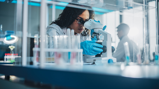 Laboratorio de Ciencias Médicas: Retrato de una hermosa científica negra que mira bajo el microscopio hace un análisis de la muestra de prueba. Ambicioso joven especialista en biotecnología, trabajando con equipos avanzados photo