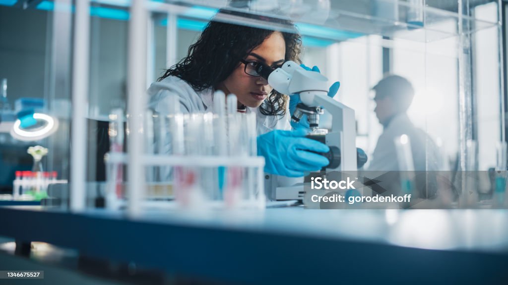Medical Science Laboratory: Portrait of Beautiful Black Scientist Looking Under Microscope Does Analysis of Test Sample. Ambitious Young Biotechnology Specialist, working with Advanced Equipment Laboratory Stock Photo