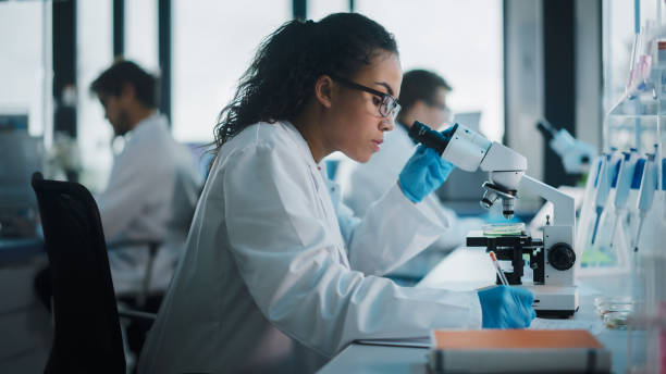 laboratorio de ciencias médicas: hermoso científico negro que mira bajo el microscopio hace análisis de muestra de prueba. equipo diverso de jóvenes especialistas, utilizando equipos de tecnología avanzada. - microscopio fotografías e imágenes de stock